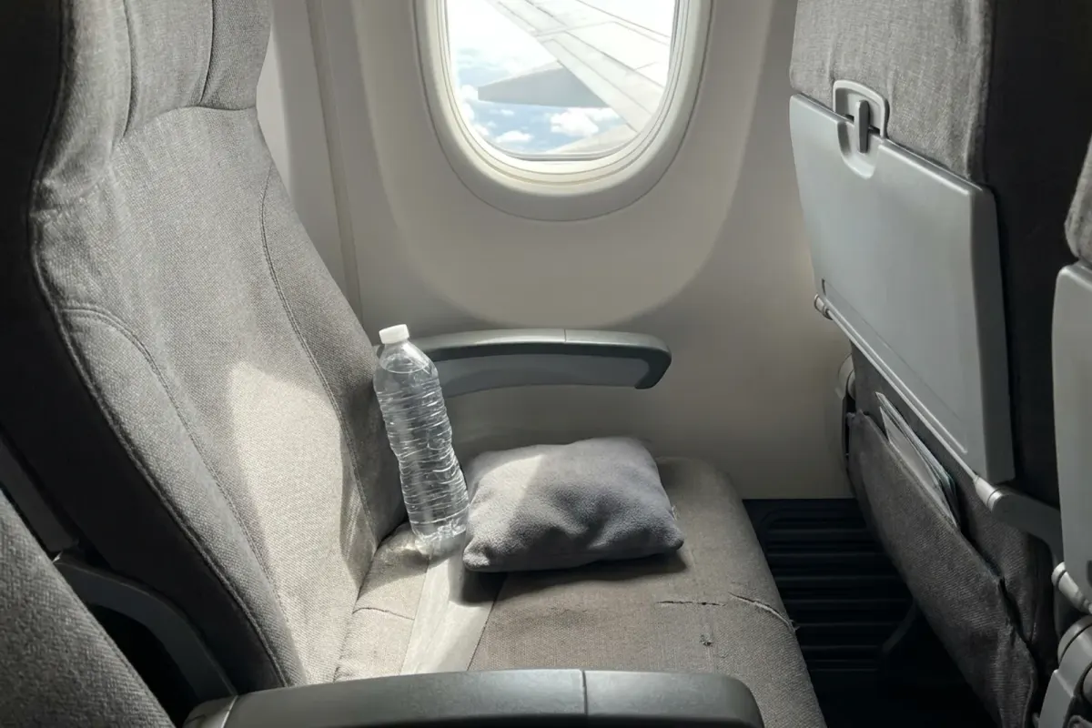 A window seat on a plane with a pillow and a bottle of water