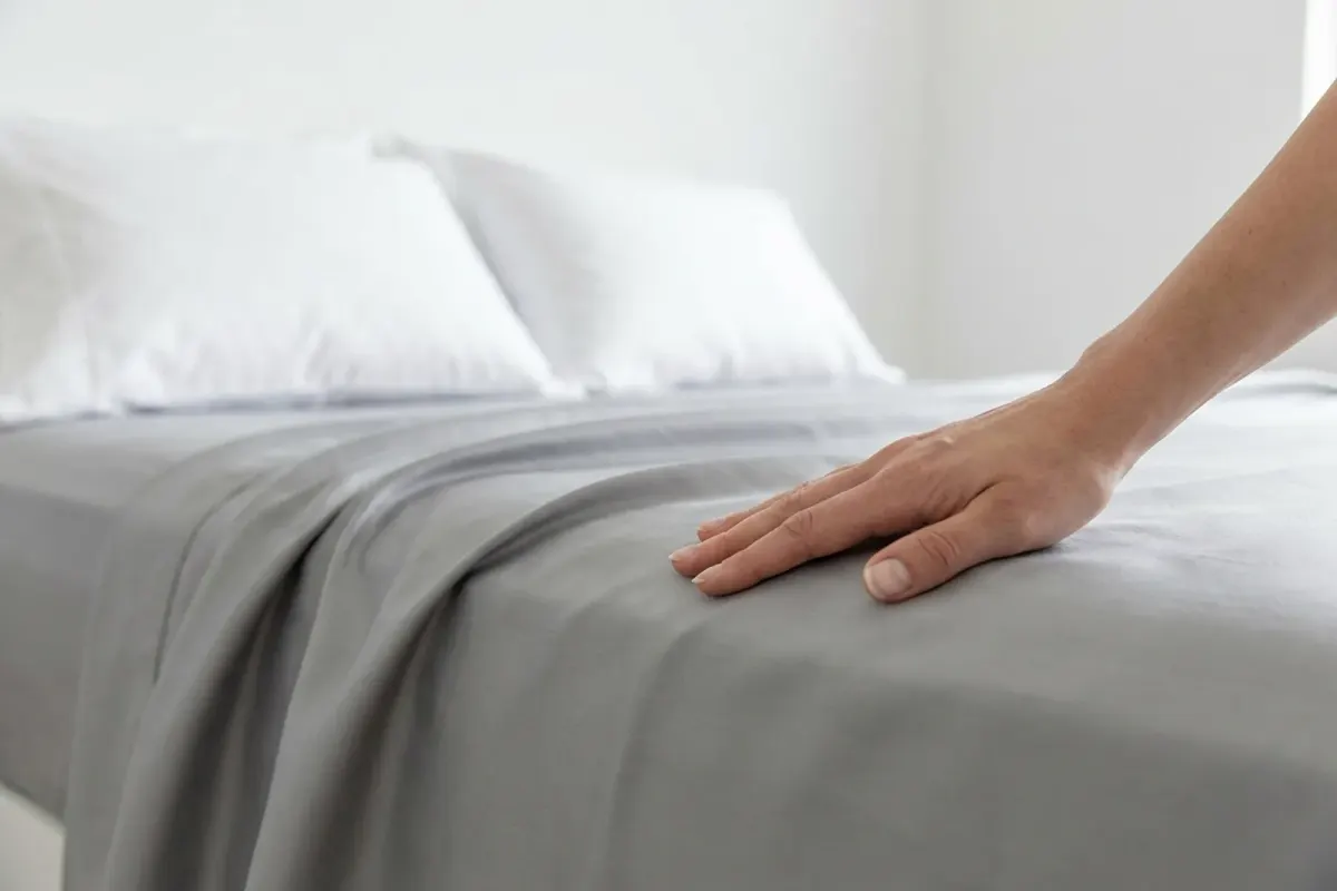A hand smoothing a soft light grey bed sheet