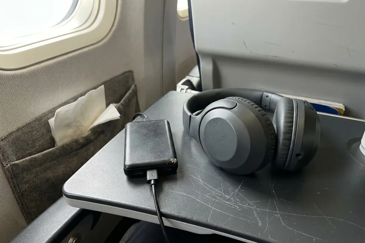 Wireless headphones and a small power bank on an airplane tray table