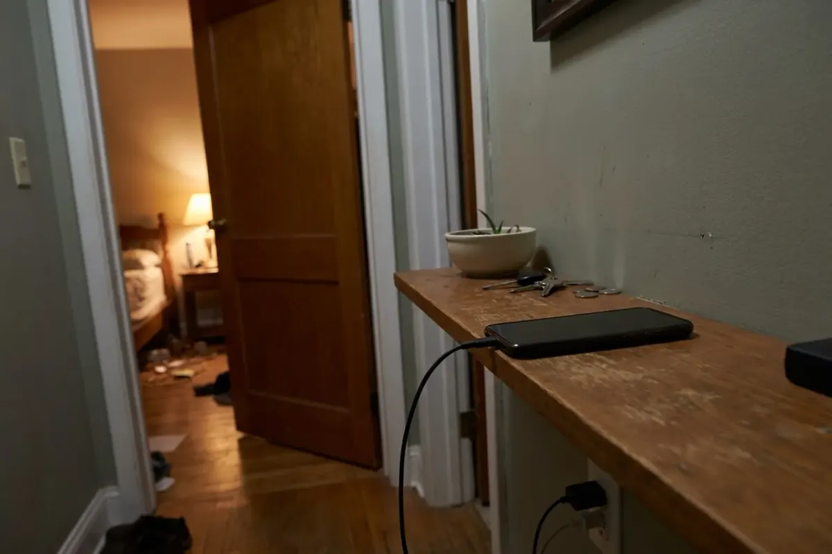 A phone charging on a hallway shelf outside a bedroom